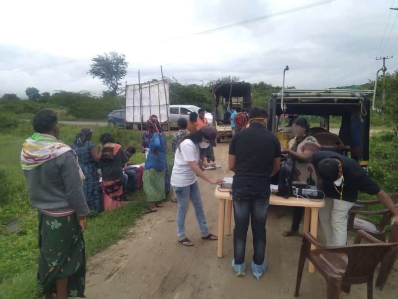 People waiting and setting up for medical field camps in a grassy field with a dirt road