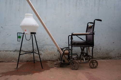 An old wheel chair, a stick, and a water holder in an empty rustic room