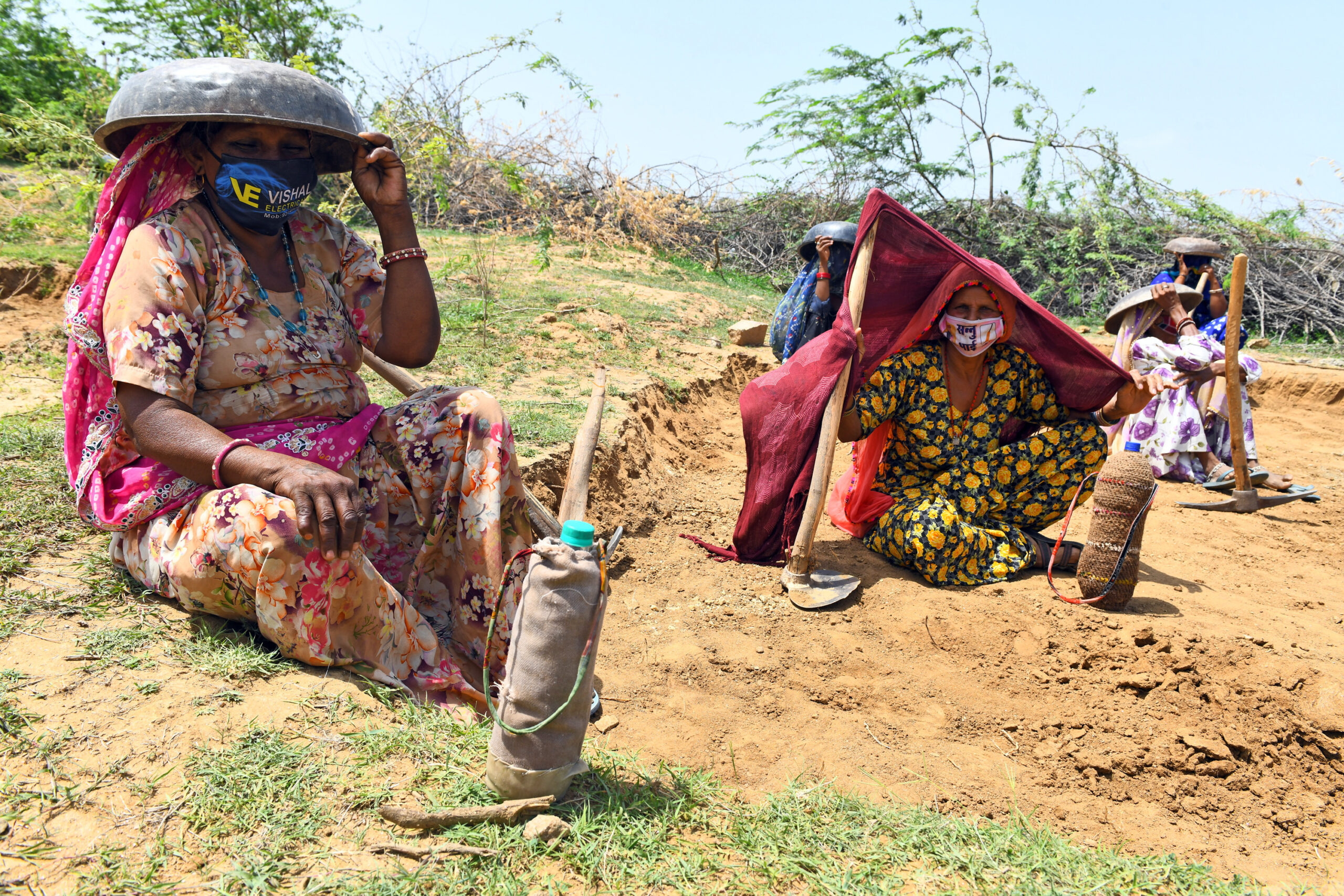 Women labourers sit under tagaris (a pan to carry loads like soil) to protect themselves against the scorching sun, as they work at a site.